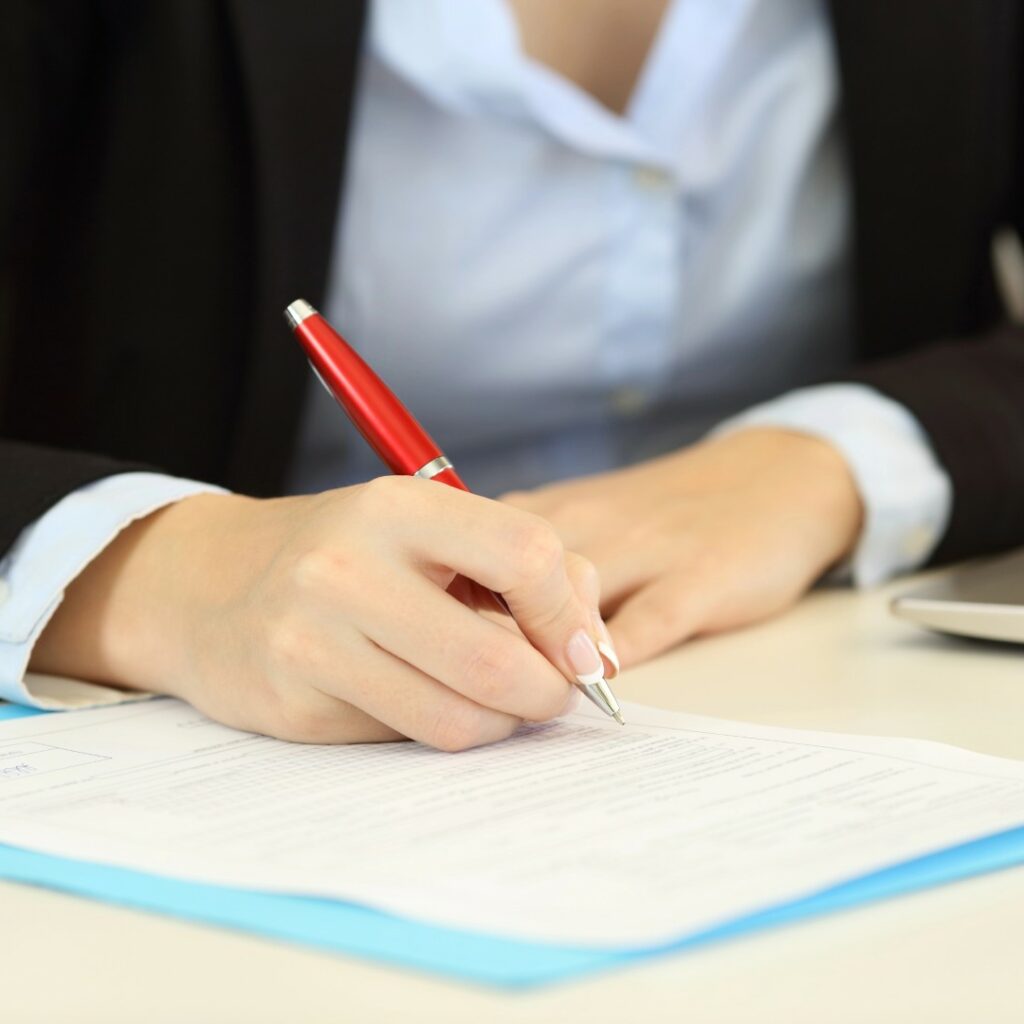 Donna in abito professionale che firma documenti accanto a un laptop