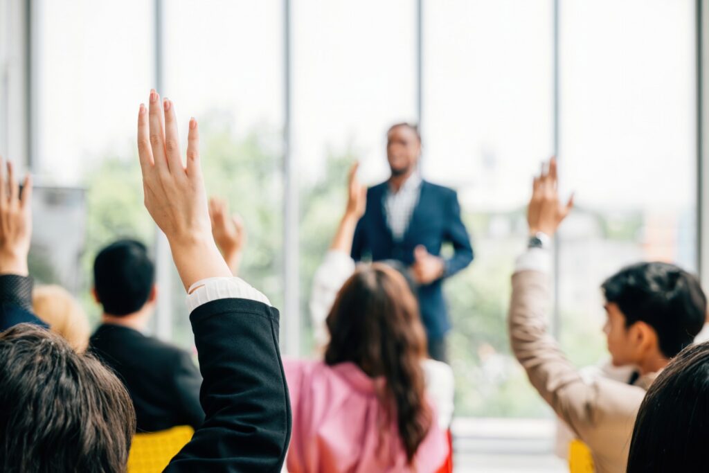 Persone che alzano la mano durante un incontro con un relatore sullo sfondo